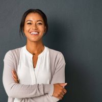 Beautiful mid adult african american woman standing on grey wall with crossed arms. Mature indian woman isolated on gray background. Portrait of smiling hispanic lady looking at camera with satisfaction.